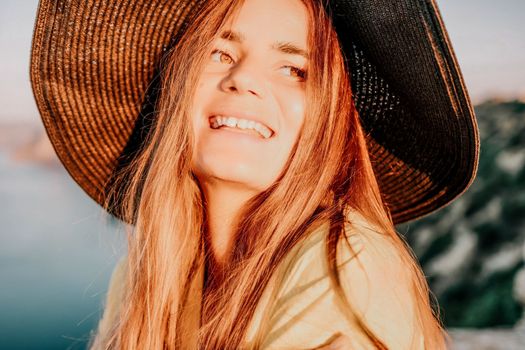 Portrait of happy young woman wearing summer black hat with large brim at beach on sunset. Closeup face of attractive girl with black straw hat. Happy young woman smiling and looking at camera at sea