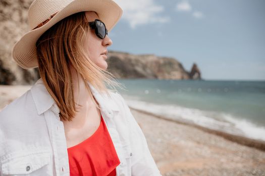 Young woman in red bikini on Beach. Blonde in sunglasses on pebble beach enjoying sun. Happy lady in one piece red swimsuit relaxing and sunbathing by turquoise sea ocean on hot summer day. Close up,