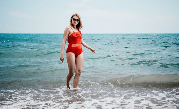 Young happy woman walks carefree on the seaside. Happy lady in red bikini. Portrait beautiful young woman relax smile around beach sea ocean in holiday vacation travel trip.