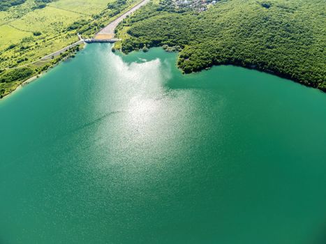 Aerial landscape from flying drone storage reservoir at mountain foot covered colorful spring forest. Beautiful view from above blue lake among highlands