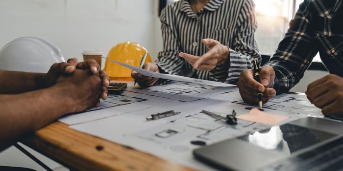 Architect and engineer team working with blueprints for architectural plan, engineer sketching a construction project, green energy concept.