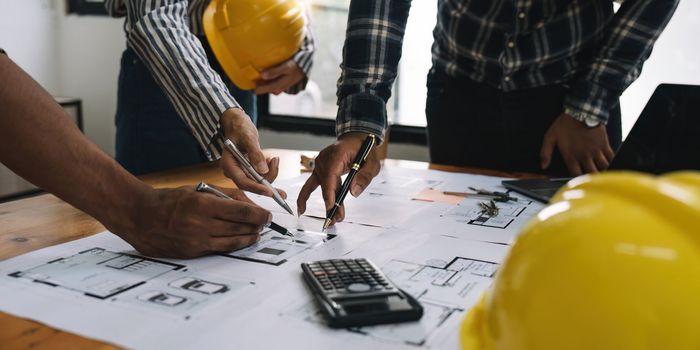 Architect and engineer team working with blueprints for architectural plan, engineer sketching a construction project, green energy concept.