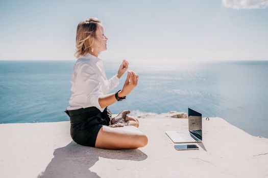 Happy girl doing yoga with laptop working at the beach. beautiful and calm business woman sitting with a laptop in a summer cafe in the lotus position meditating and relaxing. freelance girl remote work beach paradise