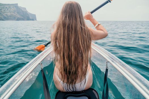 Woman in kayak back view. Happy young woman with long hair floating in transparent kayak on the crystal clear sea. Summer holiday vacation and cheerful female people having fun on the boat.