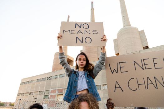 Young woman sitting on protester shoulder holding a no means no banner above her head in a feminist demonstration. Copy space. Equality and woman's right concept.