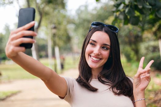 young caucasian woman taking a selfie photo for her social media with her mobile phone from a park, concept of youth and technology of communication