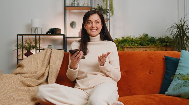 Happy brunette woman use mobile smartphone typing browsing say Wow yes found out great big win good news celebrate lottery jackpot doing winner gesture. Girl at home in living room sitting on couch