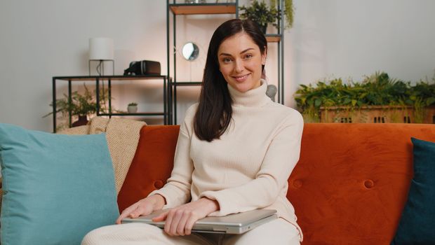 Young woman using credit bank card and laptop computer while transferring money, purchases online shopping, order food delivery at home apartment. Adult girl in day living room sitting on couch indoor