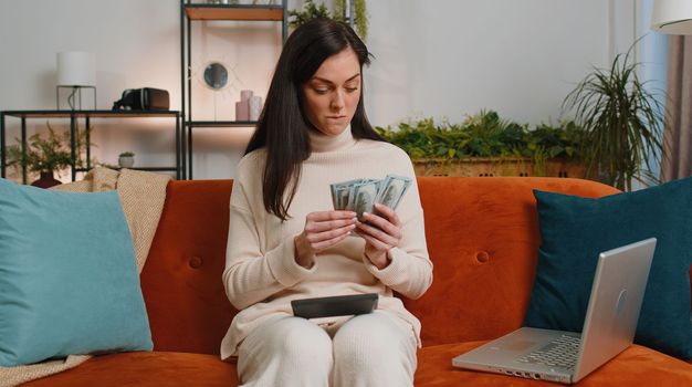 Planning budget. Rich brunette woman counting money cash use calculator and calculate domestic bills at home room. Girl satisfied of income earnings, win, saves money for planned vacation, gifts
