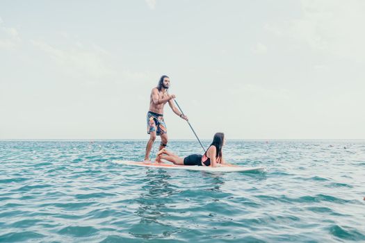 Sea woman and man on sup. Silhouette of happy young woman and man, surfing on SUP board, confident paddling through water surface. Idyllic sunset. Active lifestyle at sea or river