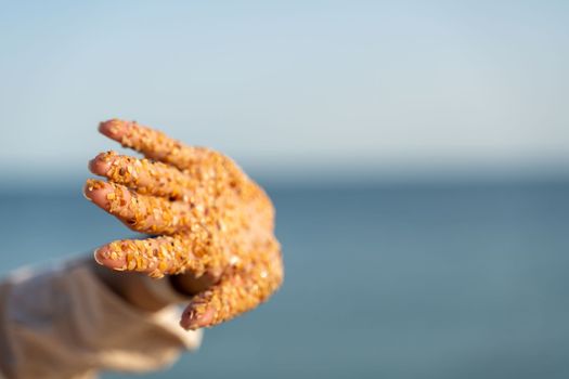 Sand hand sea. Small pieces of shells sand stuck to the palms of a woman against the backdrop of the sea and blue sky