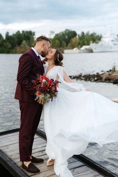 the first meeting of the bride and groom in wedding dresses on the pier near the water