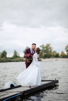 the first meeting of the bride and groom in wedding dresses on the pier near the water