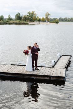 the first meeting of the bride and groom in wedding dresses on the pier near the water