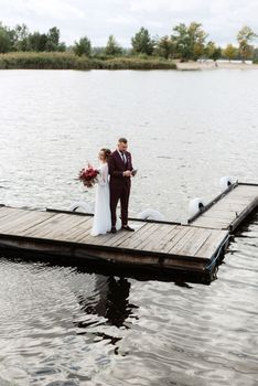 the first meeting of the bride and groom in wedding dresses on the pier near the water