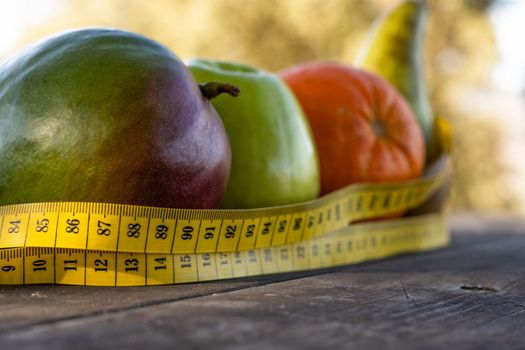 group of healthy fruit with tape measure on a wooden table illuminated by the sun