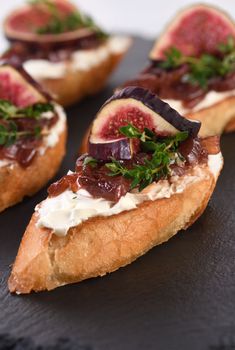 Canape or crostini with toasted baguette, cream cheese, onion jam, figs and fresh thyme on a slate board. Perfect as an aperitif for a holiday or party.