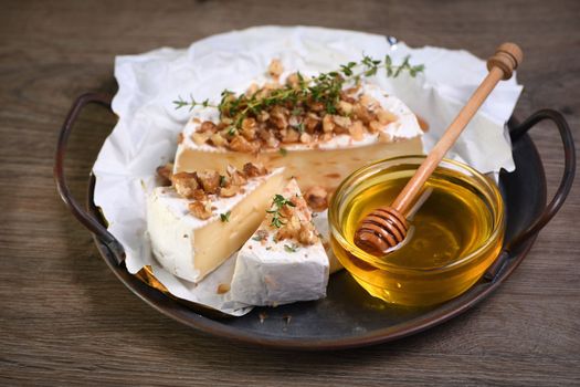 Camembert soft cheese is served on an iron dish with walnuts, honey and thyme. 