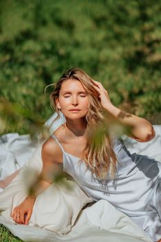 woman sleeps on a white bed in the fresh spring grass in the garden. Dressed in a blue nightgown