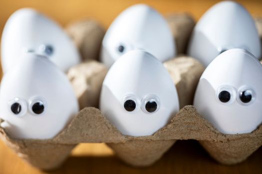 Funny faces on white eggs in carton box with organic chicken eggs on kitchen table closeup big animation eyes. humor, food and easter holiday concept. close up