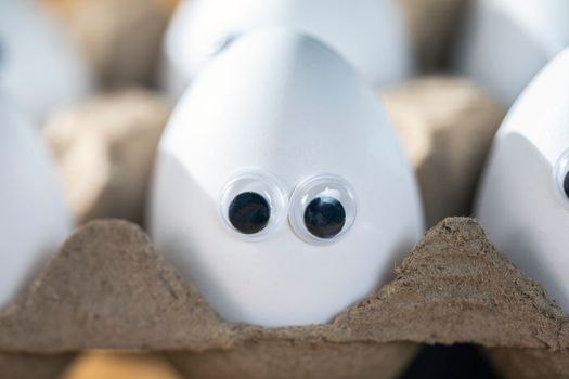 Funny faces on white eggs in carton box with organic chicken eggs on kitchen table closeup big animation eyes. humor, food and easter holiday concept. close up