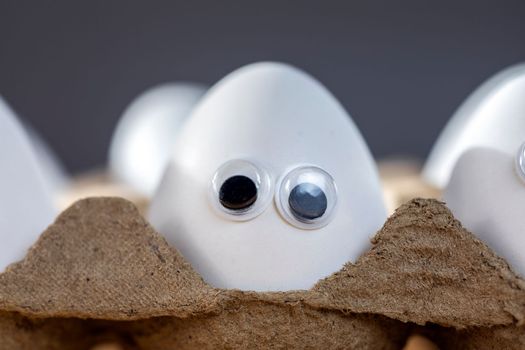 Funny faces on white eggs in carton box with organic chicken eggs on kitchen table closeup big animation eyes. humor, food and easter holiday concept. close up