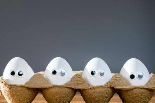 Funny faces on white eggs in carton box with organic chicken eggs on kitchen table closeup big animation eyes. humor, food and easter holiday concept. close up