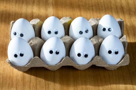 Funny faces on white eggs in carton box with organic chicken eggs on kitchen table closeup big animation eyes. humor, food and easter holiday concept. close up