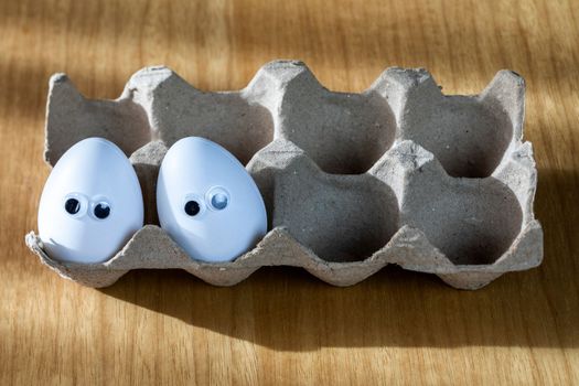 Funny faces on white eggs in carton box with organic chicken eggs on kitchen table closeup big animation eyes. humor, food and easter holiday concept. close up