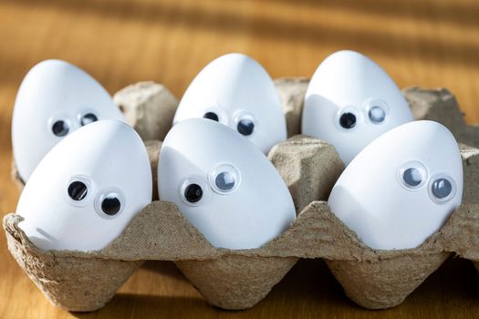 Funny faces on white eggs in carton box with organic chicken eggs on kitchen table closeup big animation eyes. humor, food and easter holiday concept. close up
