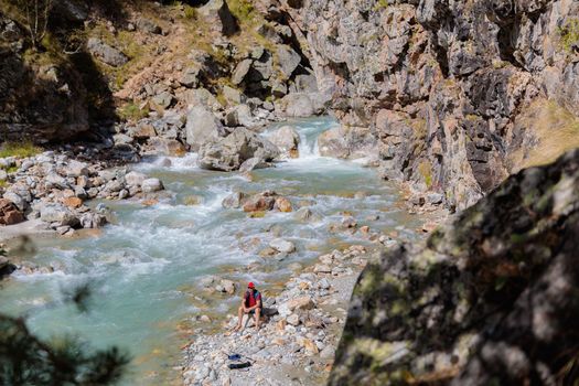 A male tourist sits by the river in the mountains. Hiking in the mountains
