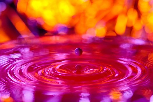 A drop falls into a dense liquid with a red background. Abstract colorful background