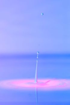 A drop falls into a thick liquid with a blue-pink background. Abstract colorful background