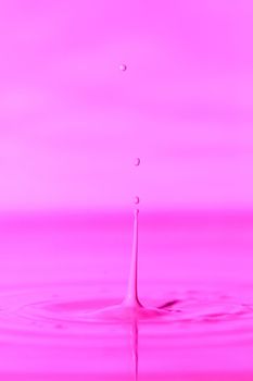 A drop falls into a thick liquid with a pink background. Abstract colorful background