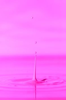 A drop falls into a thick liquid with a pink background. Abstract colorful background