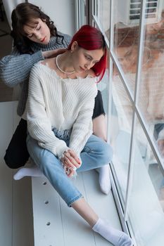 Two women dressed in sweaters sit by the window and gently hug. Lesbian intimacy