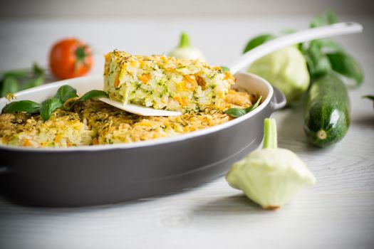vegetable casserole of patissons, zucchini, carrots in a ceramic form on a light wooden table.