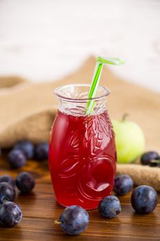 Sweet natural plum drink in a glass with a straw on a wooden table