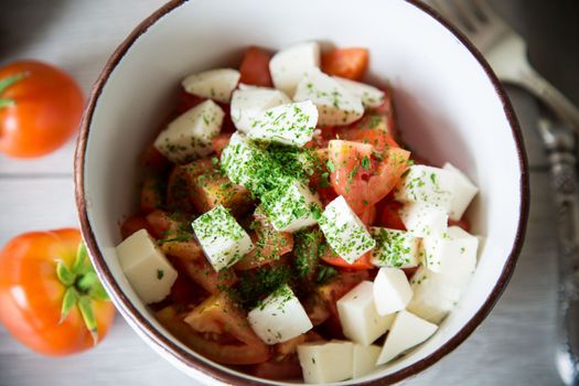 salad of fresh ripe tomatoes with mozzarella and spices in a bowl on a wooden table