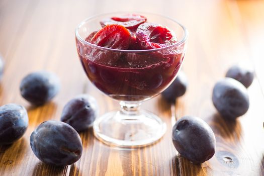 Sweet plums in syrup, in a glass bowl on a wooden table.