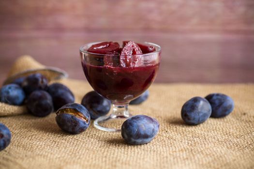 Sweet plums in syrup, in a glass bowl on a wooden table.