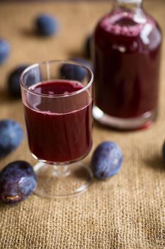 plum red wine in a glass and a decanter against the background of ripe large plums on the table.