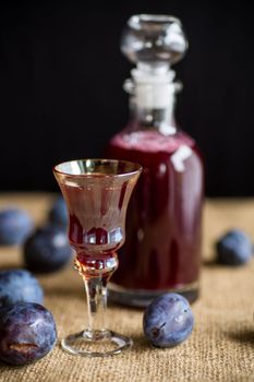 plum red wine in a glass and a decanter against the background of ripe large plums on the table.