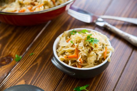 Braised cabbage with carrots, onions and herbs in a ceramic bowl on a wooden table.