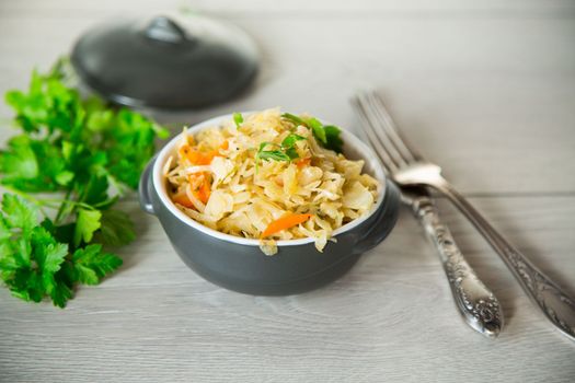 Braised cabbage with carrots, onions and herbs in a ceramic bowl on a wooden table.