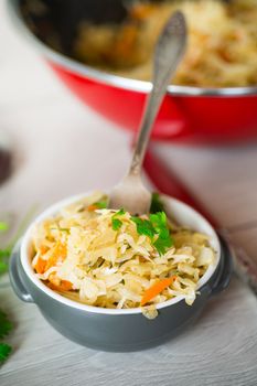 Braised cabbage with carrots, onions and herbs in a ceramic bowl on a wooden table.