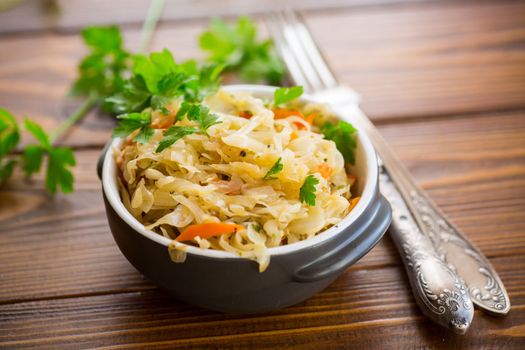 Braised cabbage with carrots, onions and herbs in a ceramic bowl on a wooden table.