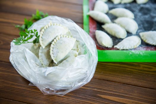 Raw green dough dumplings with parsley, dill. Raw dumplings in a bag on a wooden table.