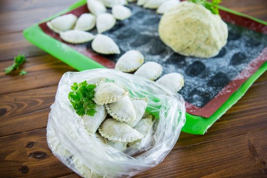 Raw green dough dumplings with parsley, dill. Raw dumplings in a bag on a wooden table.