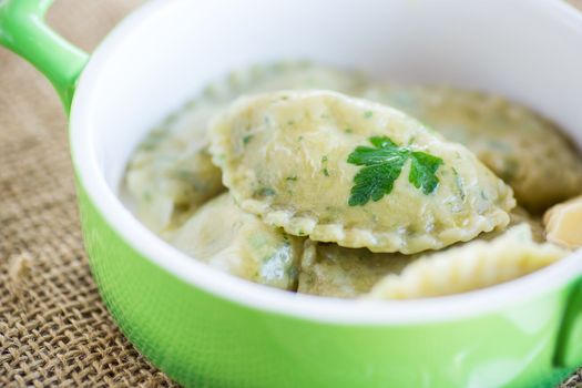 Boiled dumplings with stuffing inside, from dough with herbs in a ceramic plate.